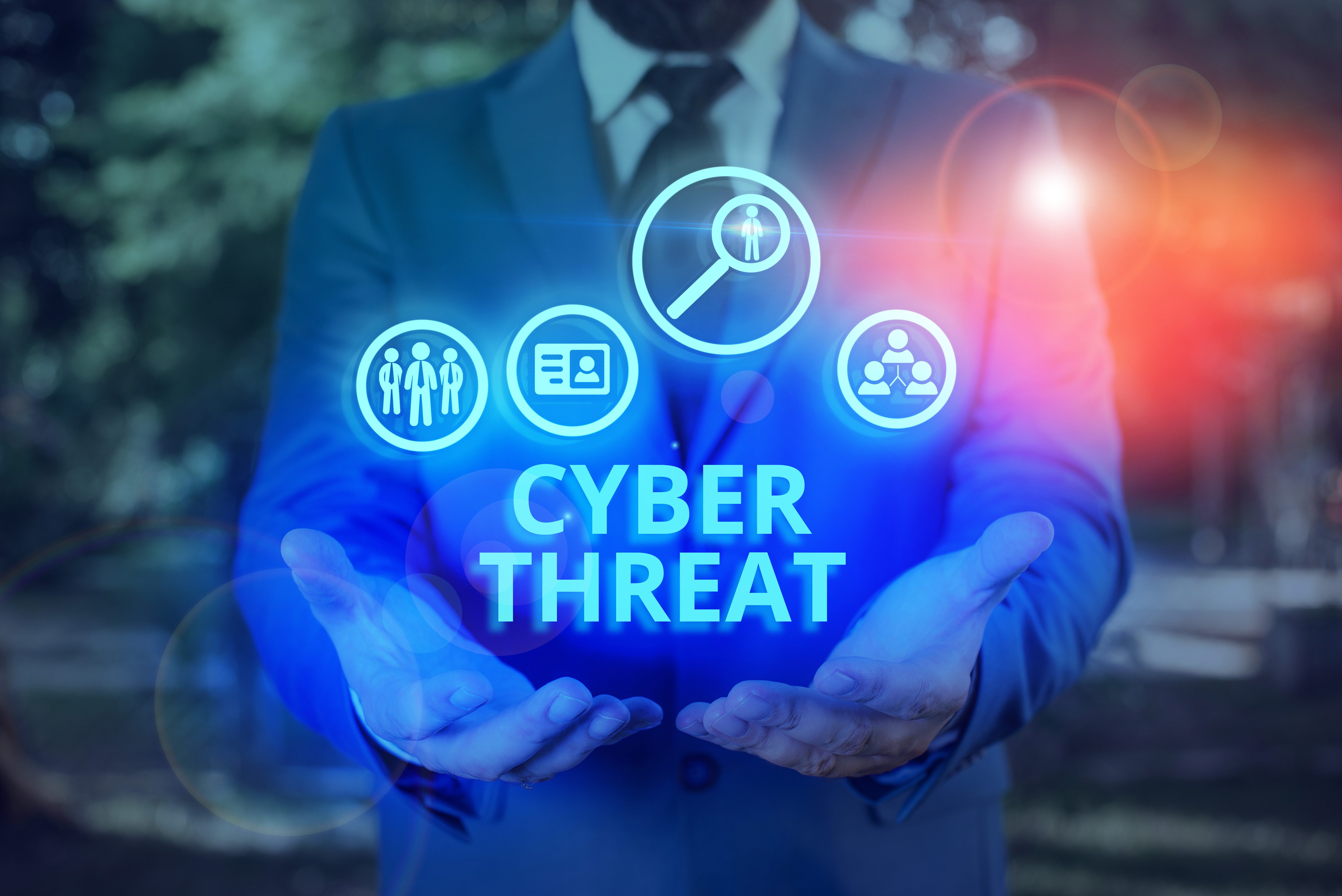 The word ‘Cyber Threat’ and icons overlaid on the overstretched palms of a man in a suit.